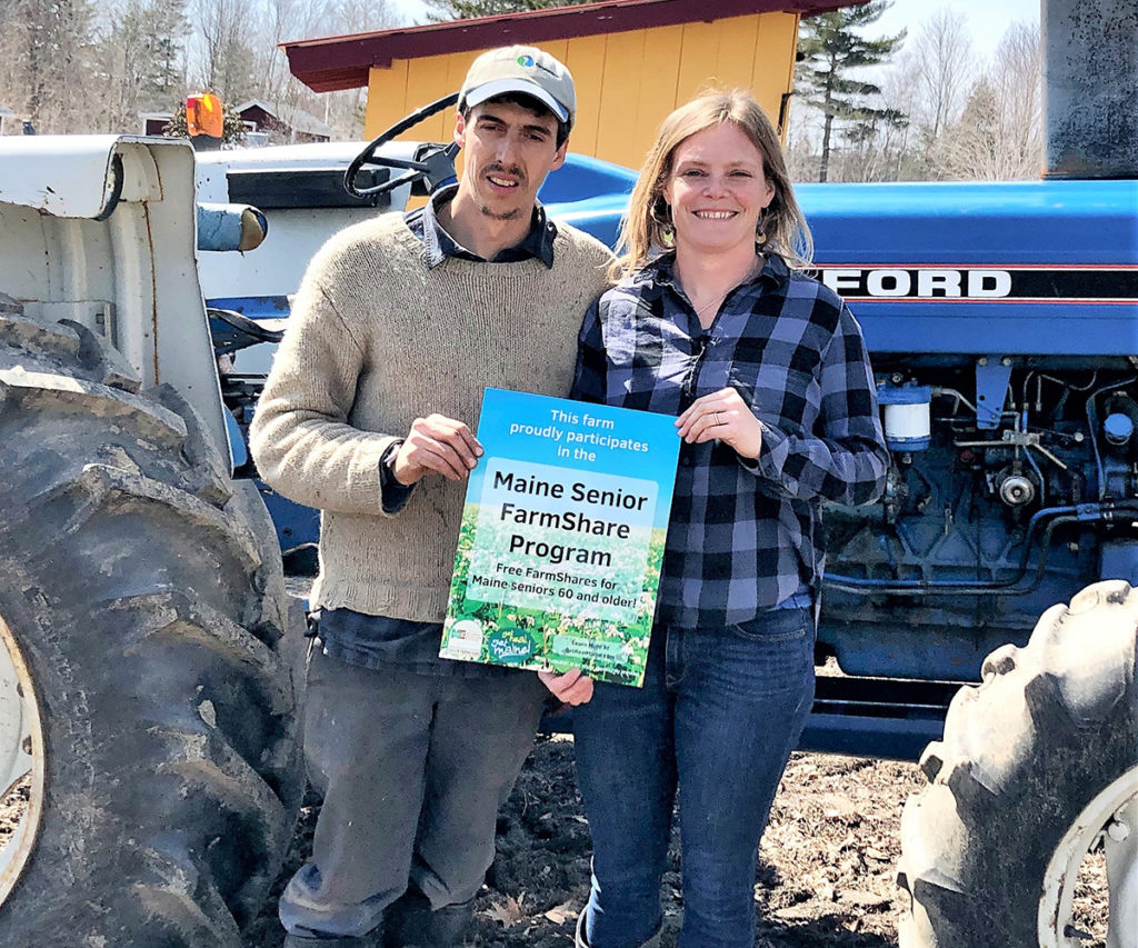 Farmers stand next to a tractor and hold a sign that shows they participate in the MSFP