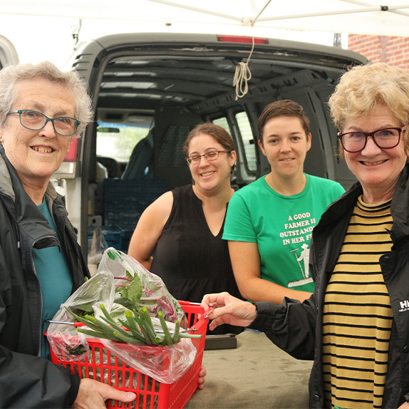 Four women at a Farmers' Market buying vegetables 