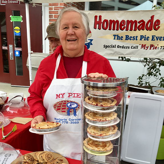 A woman standing in front of her homemade pies which can be ordered by phone